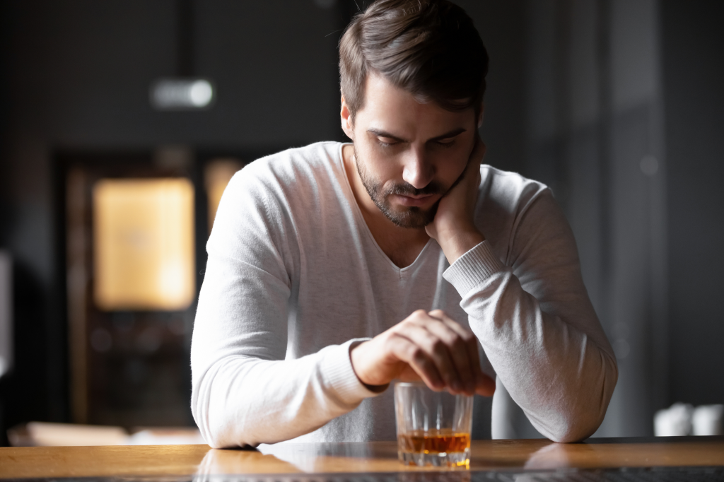 Man sitting at a bar counter looking pensively at a glass of whiskey